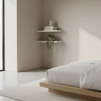 A minimalist bedroom with sleek, white floating corner shelves adorned with a few books, a small vase, and a delicate trailing plant